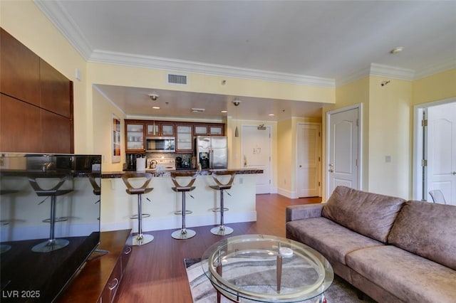 living area with ornamental molding, visible vents, dark wood finished floors, and baseboards