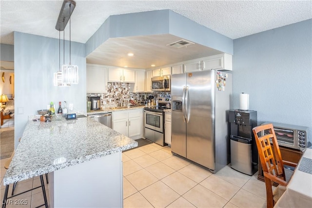 kitchen with decorative backsplash, white cabinets, light stone counters, a peninsula, and stainless steel appliances