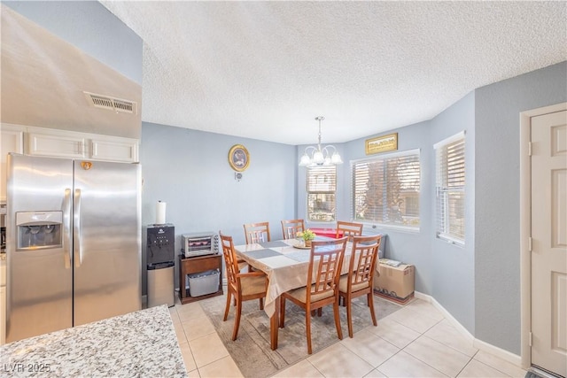 dining space with light tile patterned floors, a textured ceiling, visible vents, baseboards, and an inviting chandelier