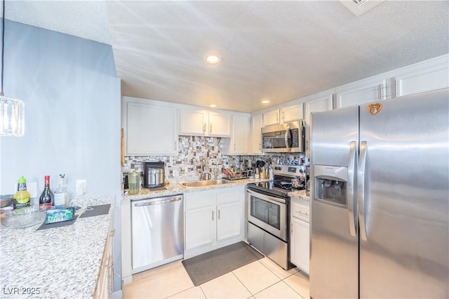 kitchen featuring light tile patterned floors, decorative backsplash, appliances with stainless steel finishes, white cabinetry, and a sink