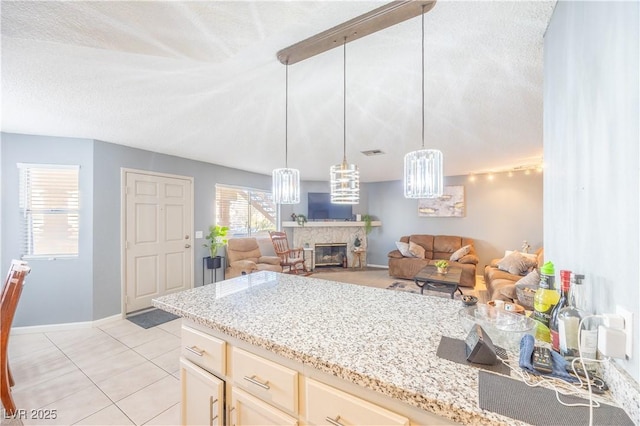 kitchen with light tile patterned floors, light stone counters, open floor plan, and a stone fireplace