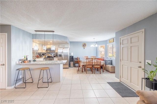 kitchen featuring stainless steel appliances, decorative light fixtures, a peninsula, and light tile patterned floors