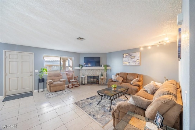 living area with visible vents, light tile patterned flooring, a stone fireplace, a textured ceiling, and baseboards