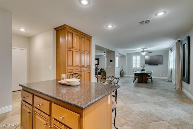 kitchen featuring brown cabinets, visible vents, a kitchen island, ceiling fan, and a kitchen bar