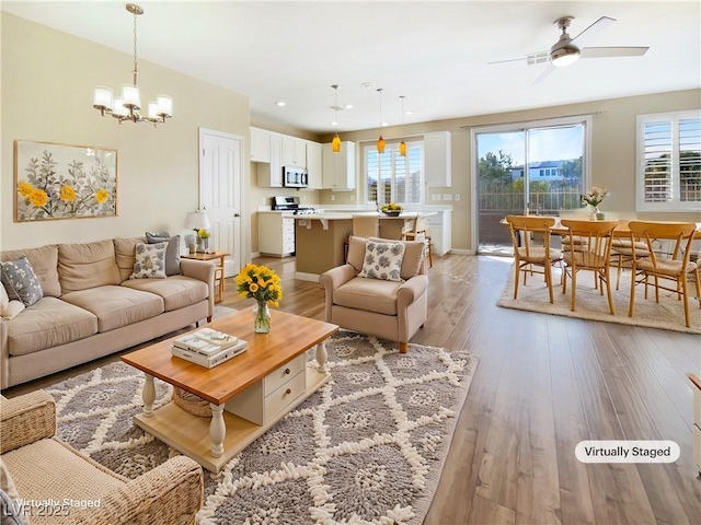 living area with light wood-style flooring, ceiling fan with notable chandelier, and a healthy amount of sunlight