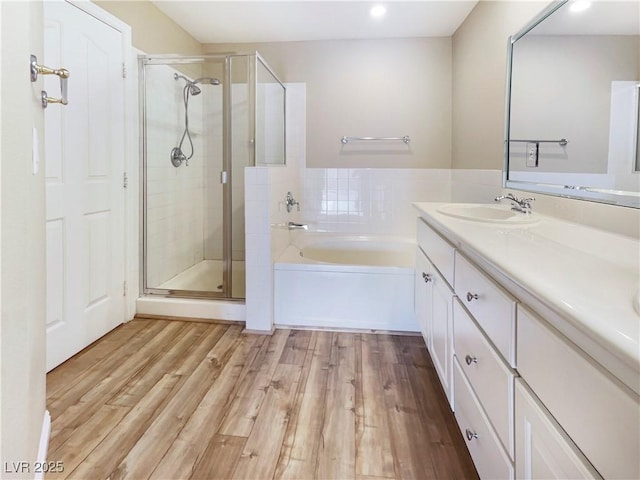 bathroom featuring a garden tub, wood finished floors, a stall shower, and a sink