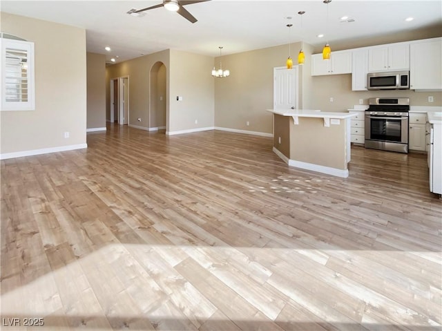 kitchen with light wood-style flooring, light countertops, stainless steel gas range oven, ceiling fan with notable chandelier, and open floor plan