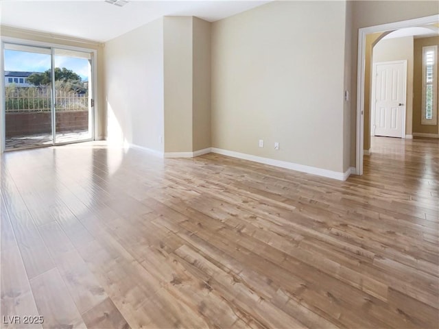 spare room with light wood-style flooring, baseboards, and arched walkways