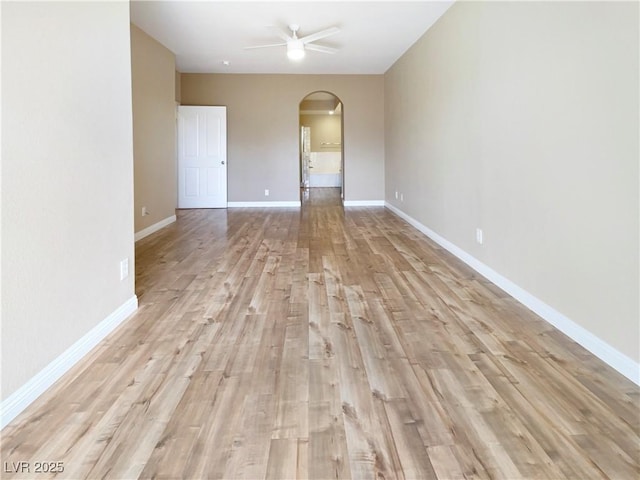 unfurnished room featuring baseboards, arched walkways, light wood-style flooring, and a ceiling fan