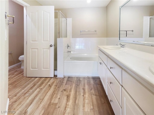 bathroom with toilet, a sink, wood finished floors, double vanity, and a bath