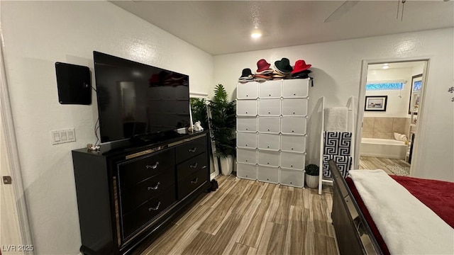 bedroom featuring ensuite bathroom, a textured wall, and light wood-style flooring