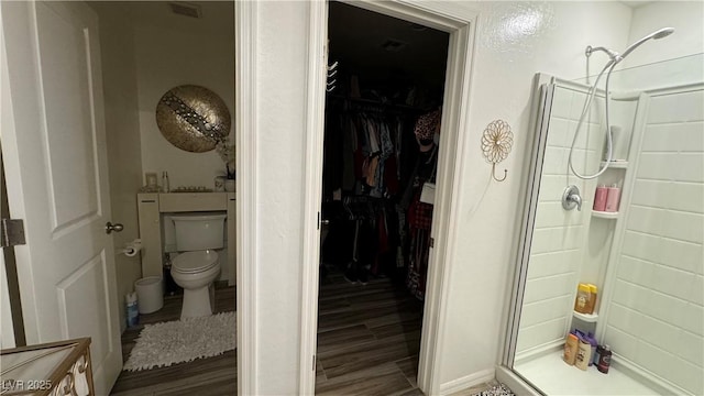 bathroom featuring wood finished floors, a shower stall, toilet, and a spacious closet