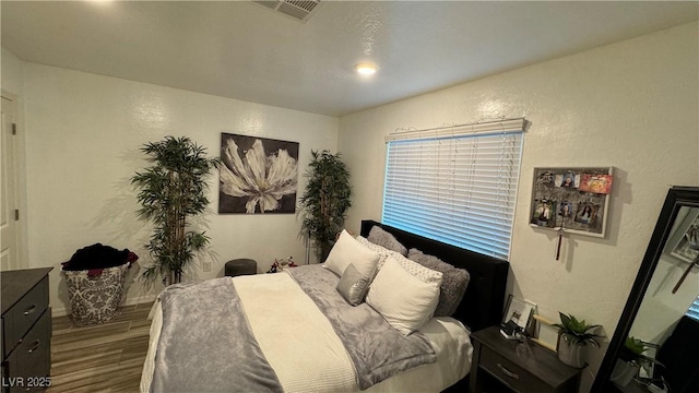 bedroom with visible vents, a textured wall, and wood finished floors