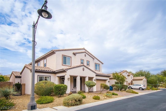 mediterranean / spanish-style house with an attached garage, fence, a tile roof, concrete driveway, and stucco siding