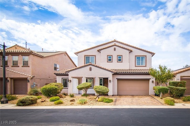 mediterranean / spanish home featuring driveway, a tiled roof, an attached garage, and stucco siding