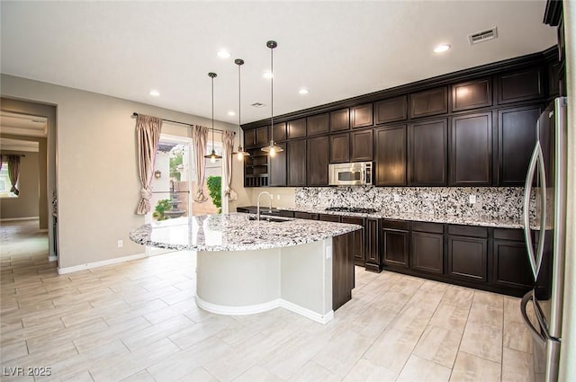 kitchen with visible vents, decorative backsplash, appliances with stainless steel finishes, light stone countertops, and a sink