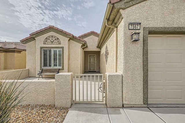 doorway to property with fence, a tiled roof, stucco siding, a garage, and a gate