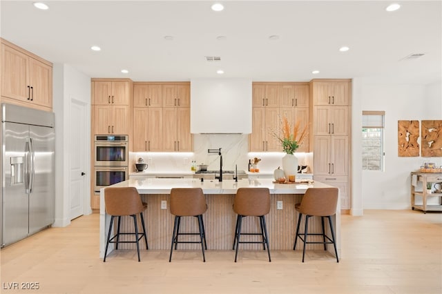 kitchen featuring light brown cabinets, stainless steel appliances, visible vents, a large island, and backsplash