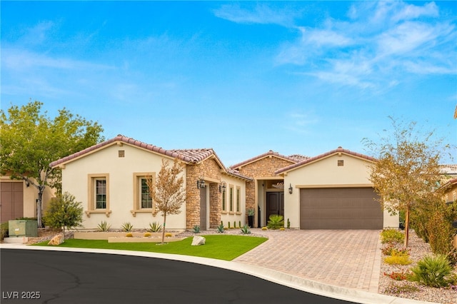 mediterranean / spanish home featuring decorative driveway, a tile roof, stucco siding, an attached garage, and stone siding