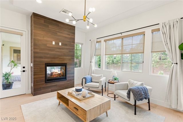 living area with a chandelier, light wood-style flooring, a multi sided fireplace, visible vents, and baseboards