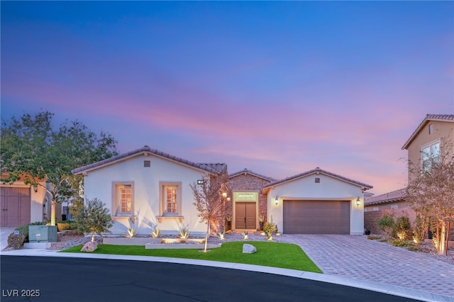 mediterranean / spanish-style home with a garage, a tile roof, decorative driveway, and stucco siding