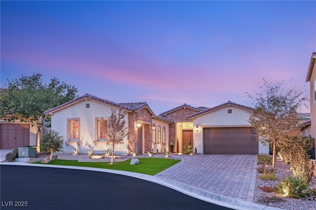 mediterranean / spanish home with stone siding, decorative driveway, an attached garage, and stucco siding