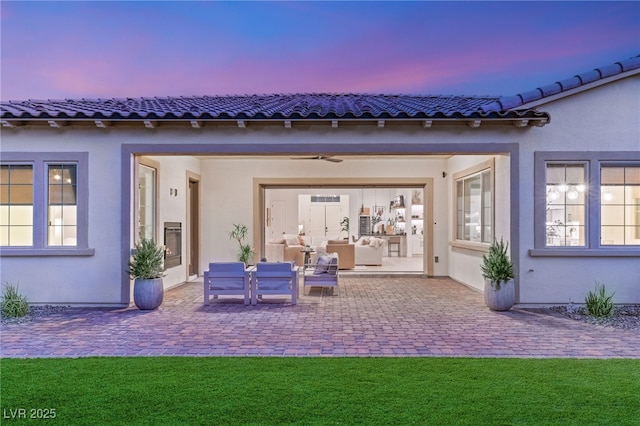 back of property at dusk with stucco siding, an outdoor hangout area, a lawn, and a patio