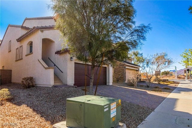 view of side of property with stucco siding, a tiled roof, decorative driveway, and a garage