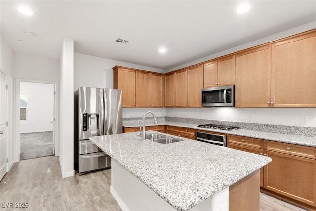 kitchen with visible vents, a center island with sink, a sink, stainless steel appliances, and light wood finished floors