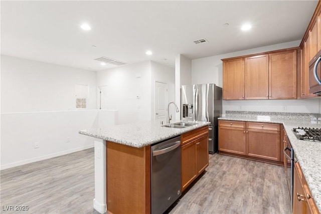 kitchen with light wood-type flooring, visible vents, a center island with sink, a sink, and stainless steel appliances