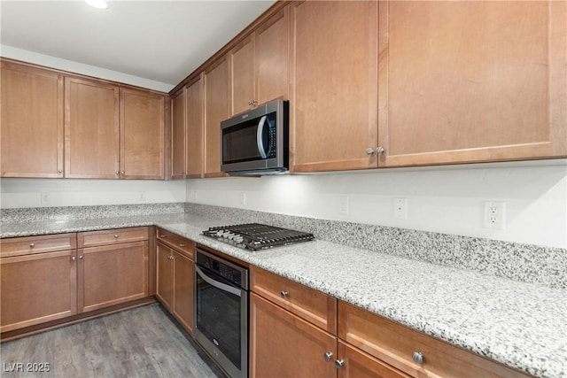 kitchen featuring light stone countertops, light wood-style floors, appliances with stainless steel finishes, and brown cabinets