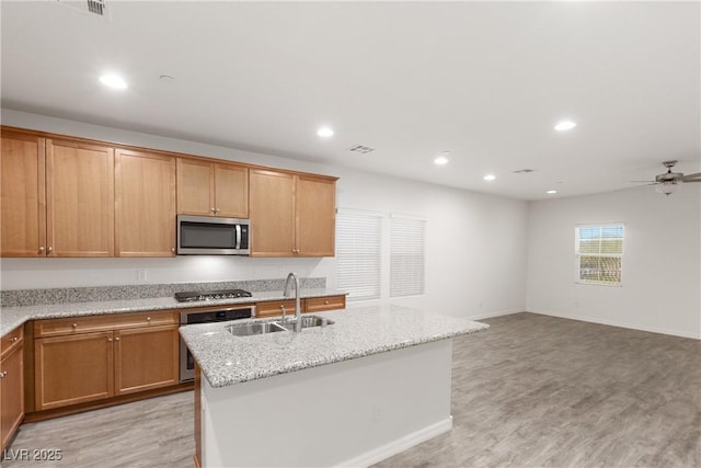 kitchen with light wood-type flooring, a center island with sink, a sink, recessed lighting, and appliances with stainless steel finishes