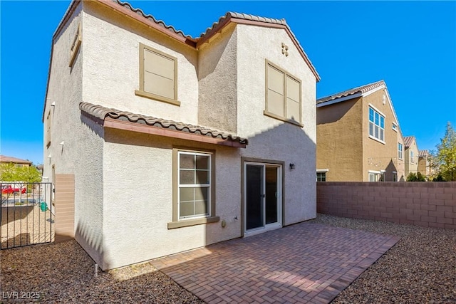 rear view of house featuring a tiled roof, stucco siding, a patio, and fence