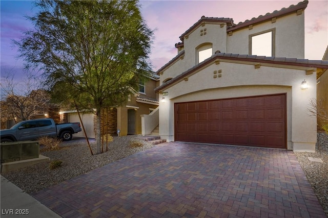 mediterranean / spanish house featuring a tiled roof, decorative driveway, and stucco siding