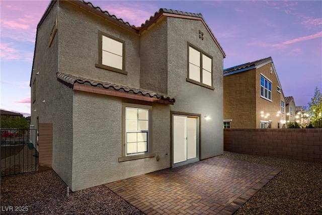 rear view of property with a tile roof, a patio area, fence, and stucco siding