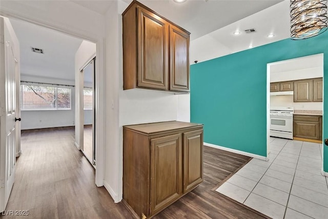 kitchen with visible vents, light wood-style floors, white range with gas cooktop, under cabinet range hood, and baseboards