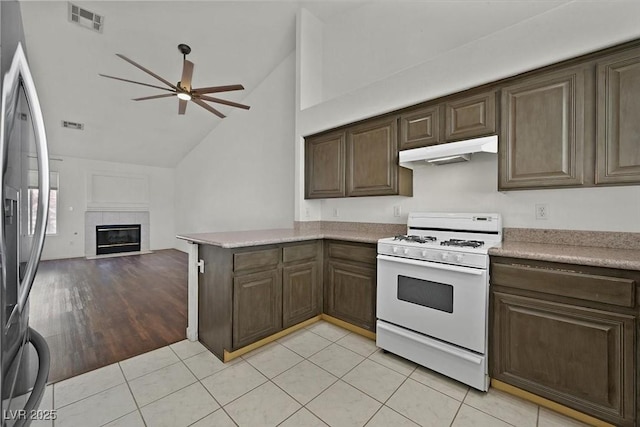 kitchen featuring under cabinet range hood, white gas range, visible vents, stainless steel fridge with ice dispenser, and a tiled fireplace