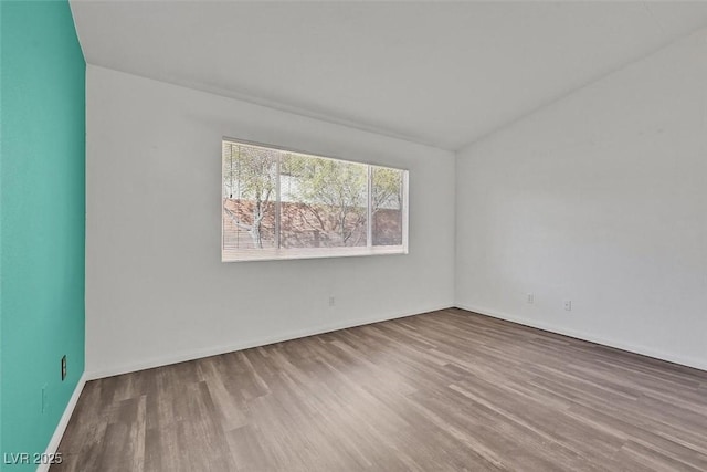 empty room featuring baseboards, vaulted ceiling, and wood finished floors