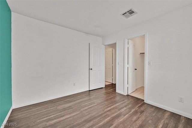 empty room featuring wood finished floors, visible vents, and baseboards