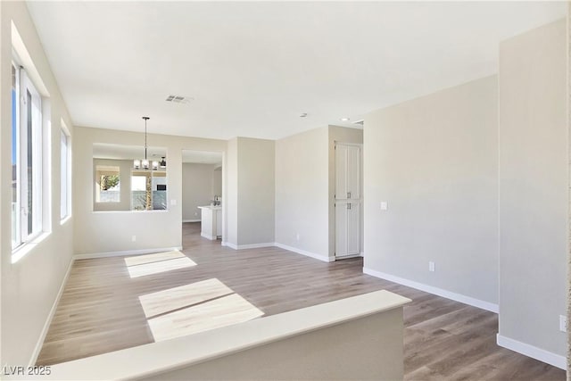 spare room featuring a notable chandelier, visible vents, baseboards, and light wood finished floors