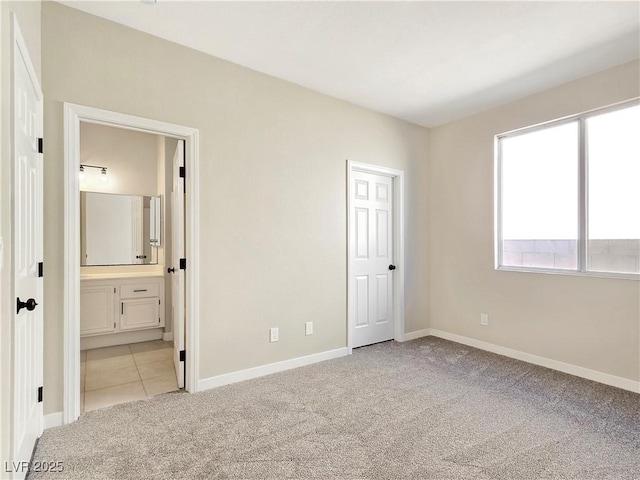 unfurnished bedroom featuring light tile patterned floors, light colored carpet, connected bathroom, and baseboards