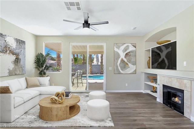 living area featuring visible vents, built in shelves, a tiled fireplace, wood finished floors, and ceiling fan