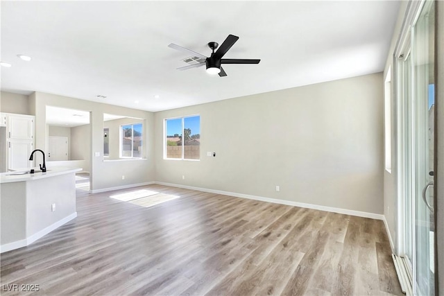 unfurnished living room with visible vents, light wood-style floors, baseboards, and a sink