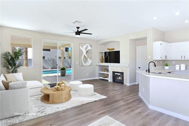 living area featuring visible vents, built in shelves, baseboards, a fireplace, and wood finished floors