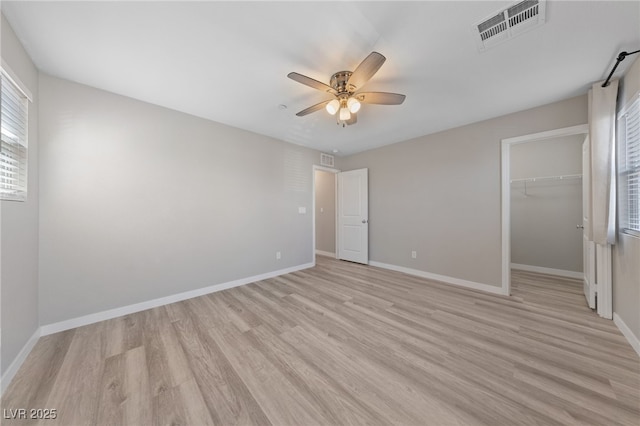 unfurnished bedroom with light wood-style flooring, a walk in closet, visible vents, and baseboards