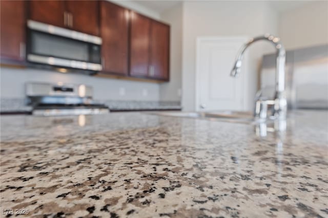 kitchen with light stone counters, stainless steel microwave, and range