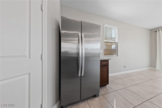 kitchen featuring dark brown cabinets, light stone counters, freestanding refrigerator, baseboards, and light tile patterned floors