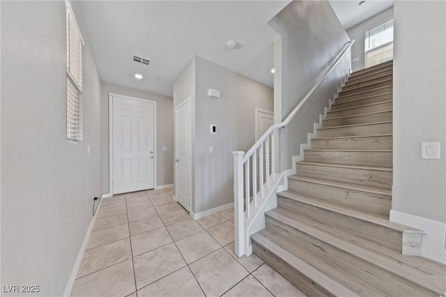 foyer featuring stairway, light tile patterned flooring, visible vents, and baseboards