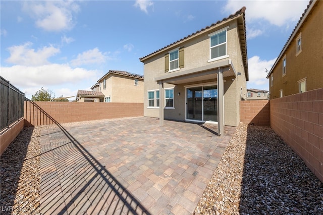 rear view of house with a tiled roof, a patio area, a fenced backyard, and stucco siding