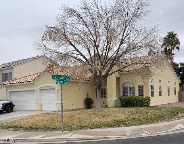 mediterranean / spanish-style home featuring a tile roof, stucco siding, an attached garage, driveway, and a front lawn